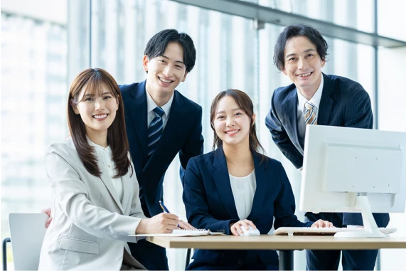 パソコンを囲みながら笑顔で仕事をする4人の社員